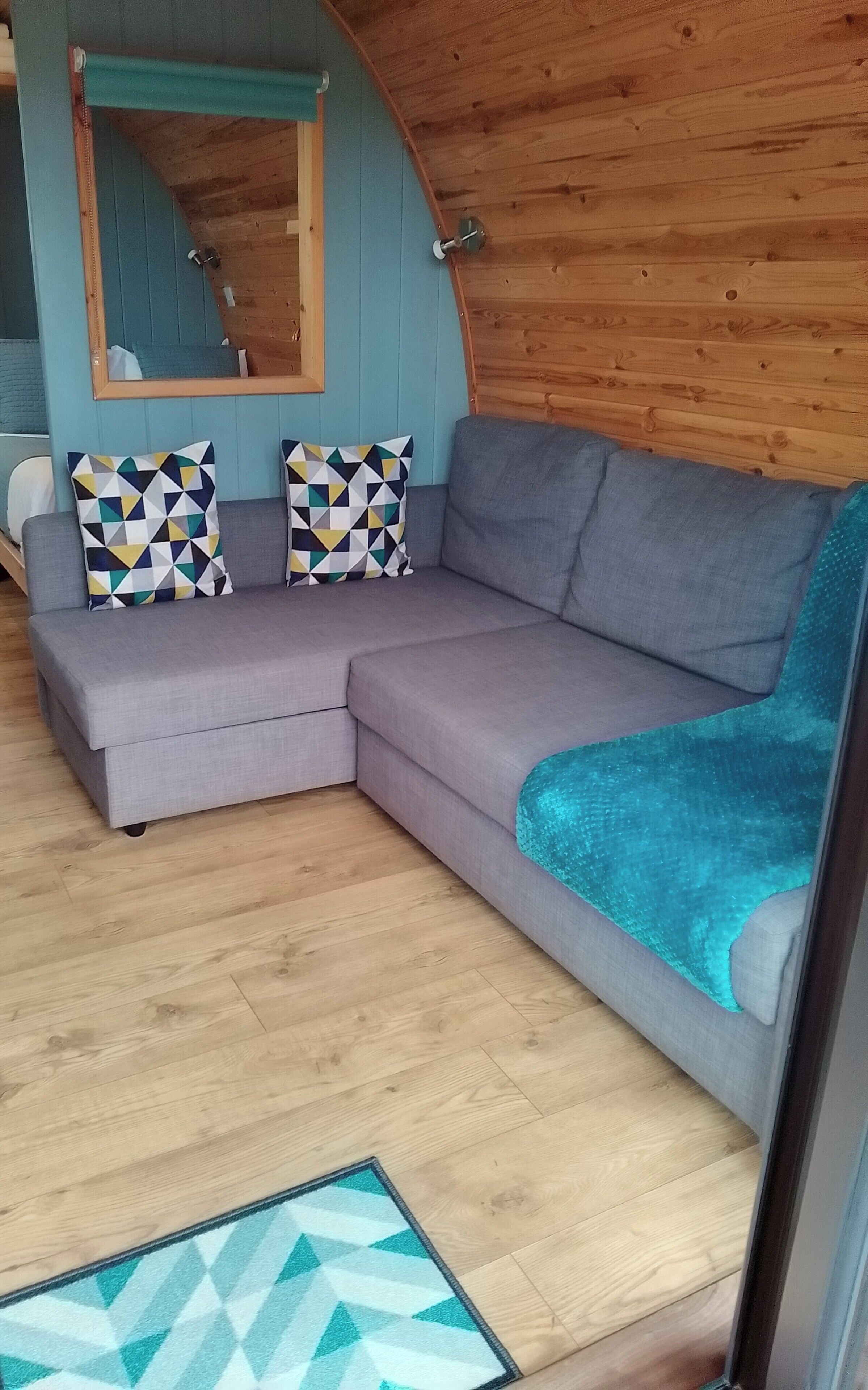 A cozy room with a gray sectional sofa, two patterned throw pillows, a teal blanket, and a wooden ceiling.