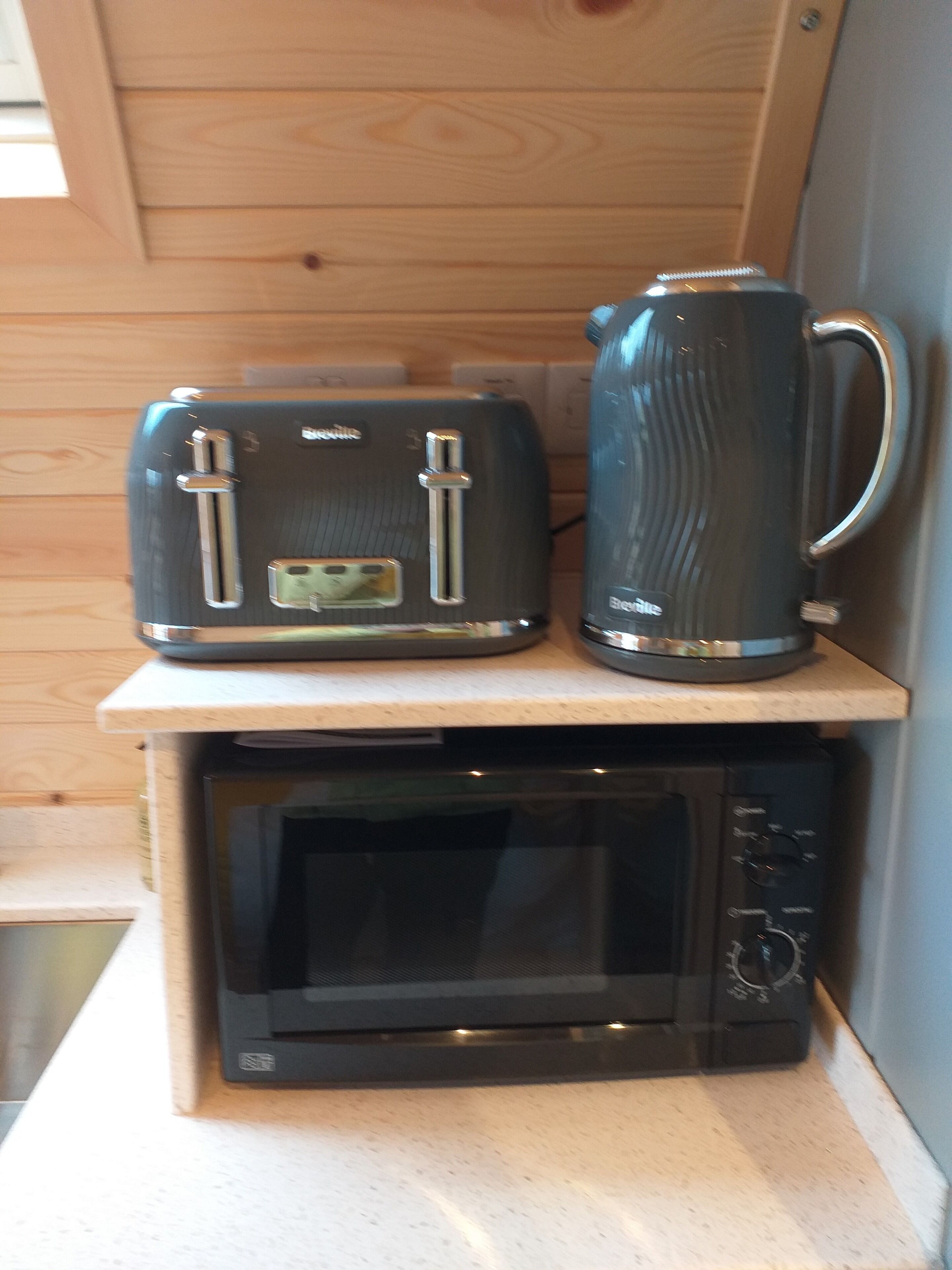 A compact kitchen setup with a microwave, a toaster, and a kettle on a countertop.