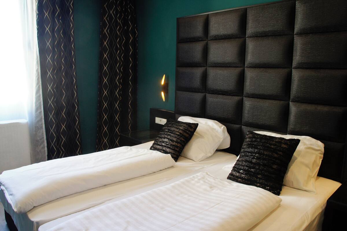 A double bed with white linens and black decorative pillows, a dark headboard, and a wall-mounted light fixture.