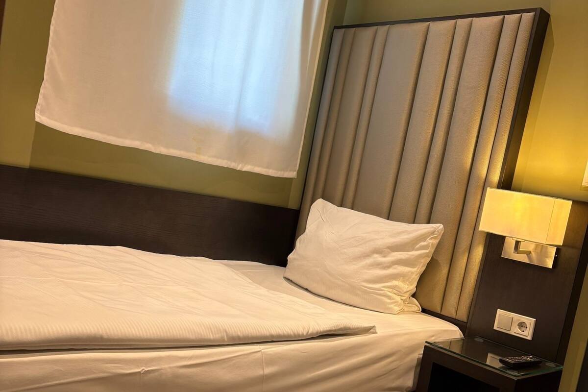 A hotel room with a bed, a nightstand, a lamp, and a window with curtains.