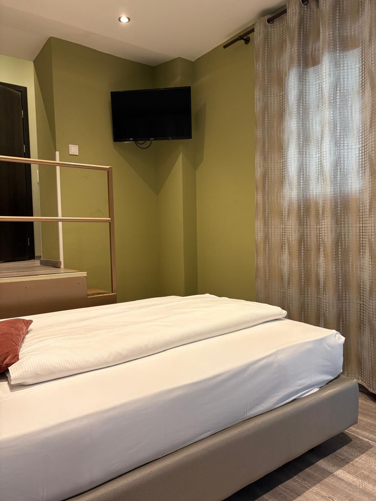 A bedroom with a bed, a TV mounted on the wall, and a window with curtains.