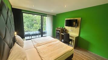 Een moderne hotelkamer met een groot bed, een bureau met stoel, een flatscreen televisie aan de muur en een balkon met zitgelegenheid.