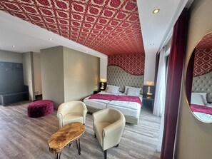 A modern hotel room with a large bed, two armchairs, a wooden coffee table, and a mirror. - Hotel Athen Kelsterbach Airport (Kelsterbach)
