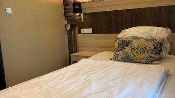 A neatly made bed with a pillow, a nightstand with a lamp, and a wall clock.