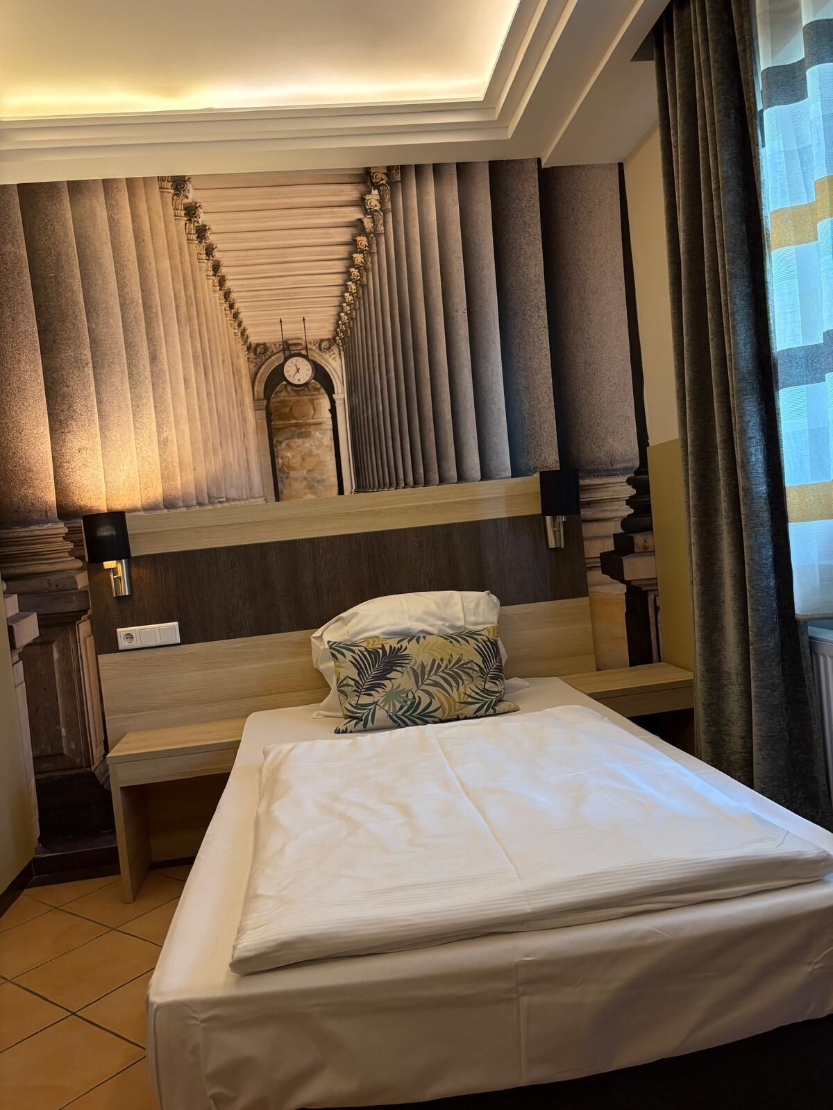 Ein Hotelzimmer mit einem großen Bett, einem Kopfteil mit vertikalen Paneelen, einer Wanduhr und einem Spiegel.