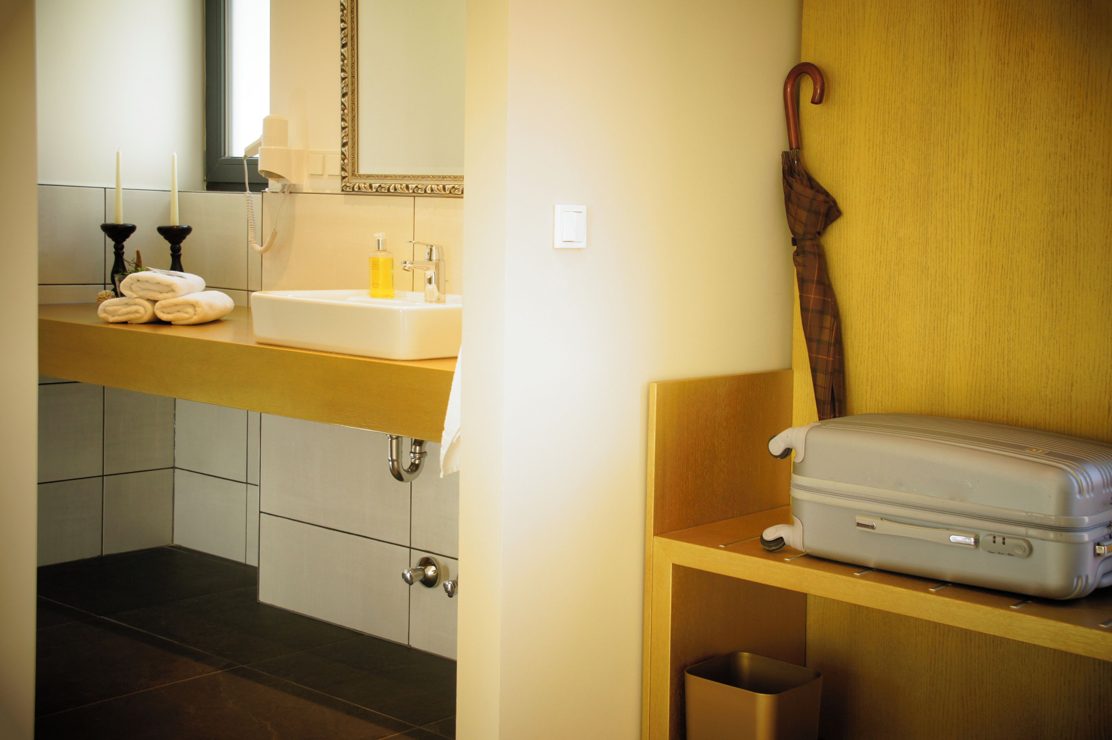 A bathroom with a sink, mirror, towel rack, and a suitcase on a shelf.