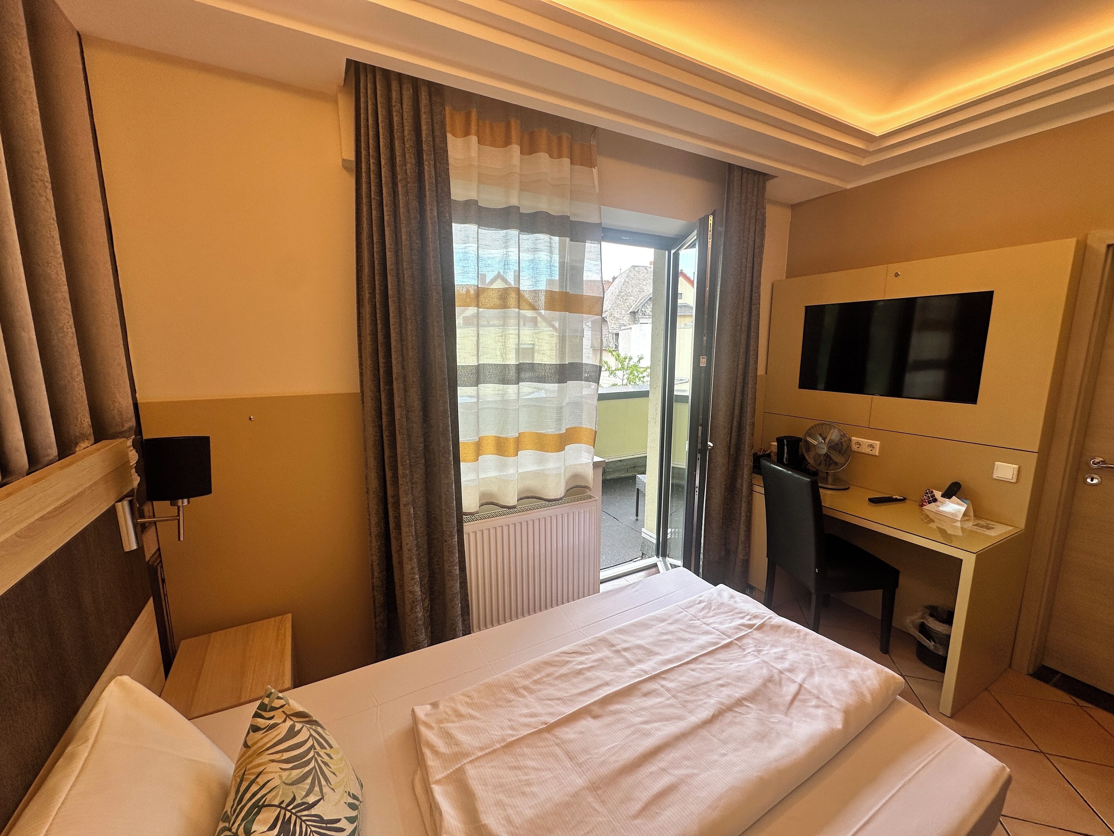 A hotel room with a bed, a desk, a TV, and a view of the outside.