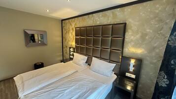 Une chambre d’hôtel avec un grand lit, une tête de lit à motifs rembourrés, des lampes de chevet et un miroir au mur.