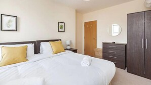 Une chambre d’hôtel bien rangée, avec un lit, une table de chevet, une lampe, une armoire et une porte.