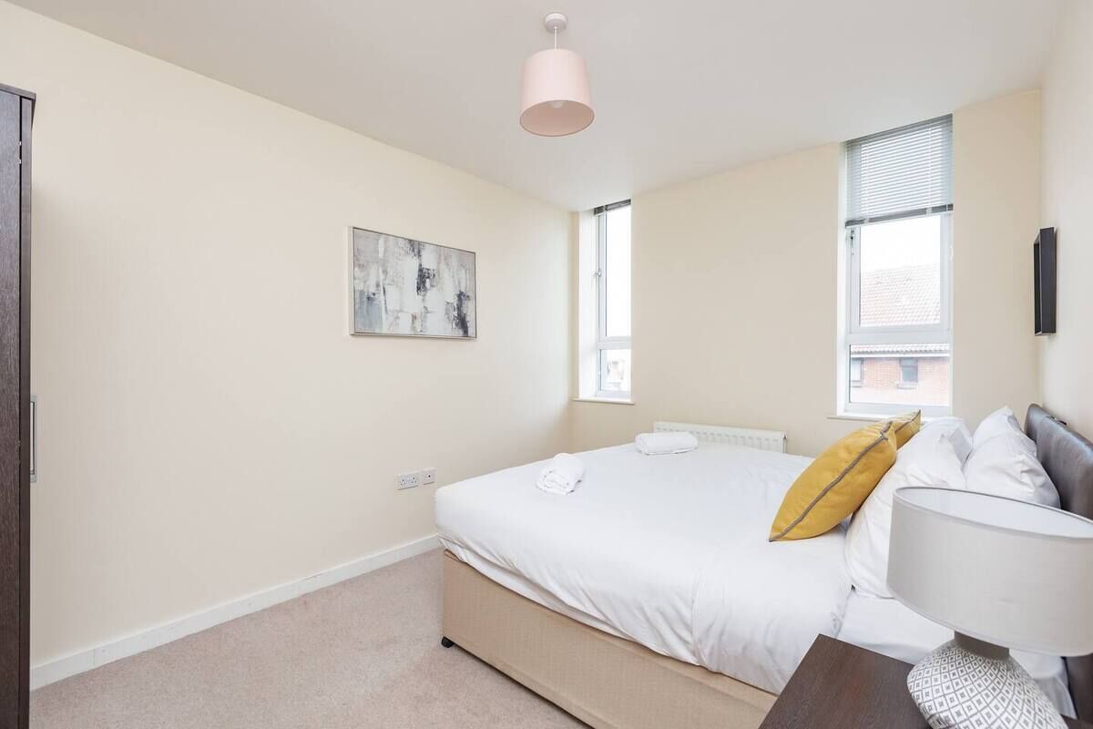 A bedroom with a bed, a bedside table, a lamp, a window, and a painting on the wall.