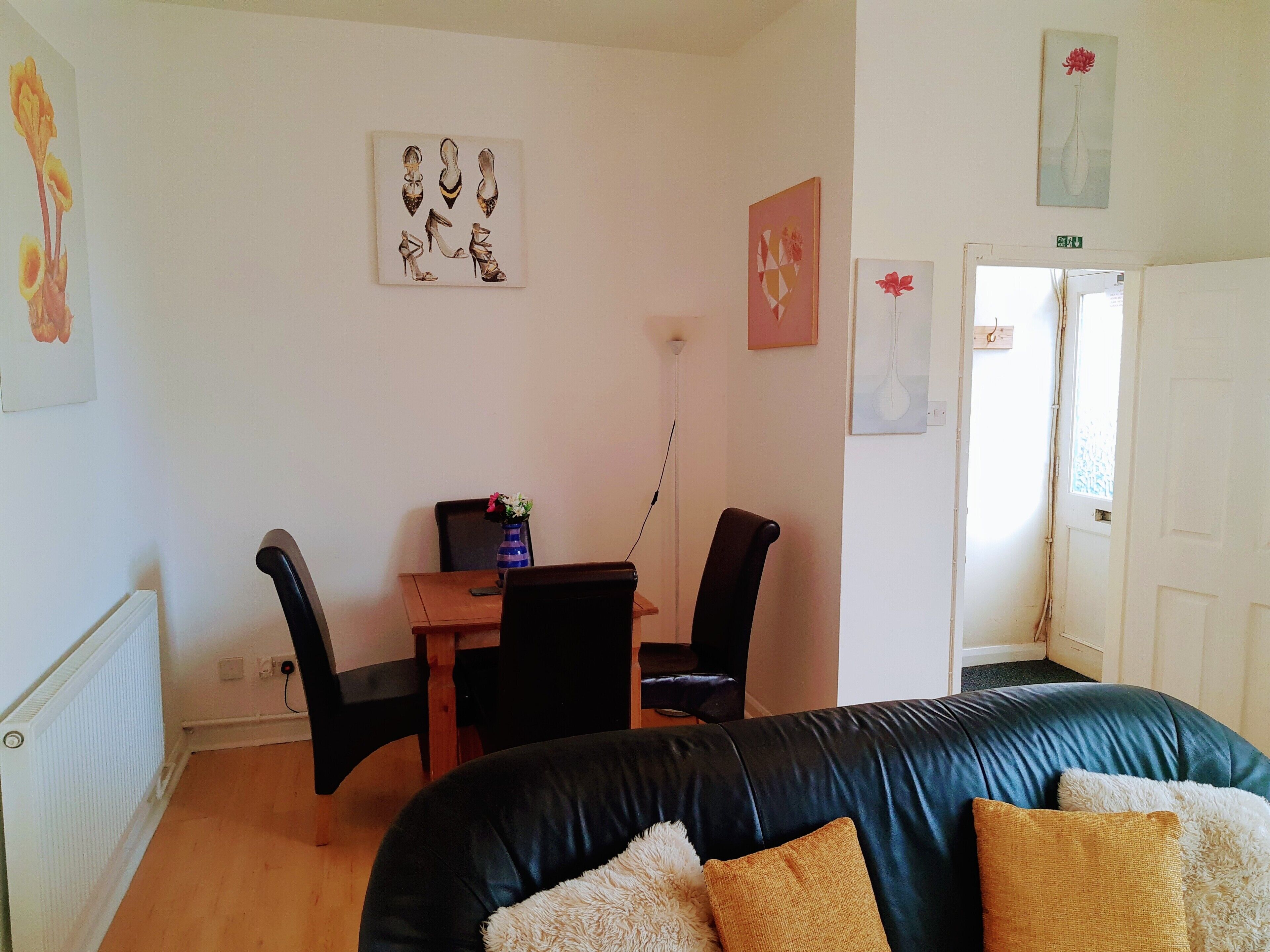 A room with a black leather sofa, a wooden table with chairs, and artwork on the walls.