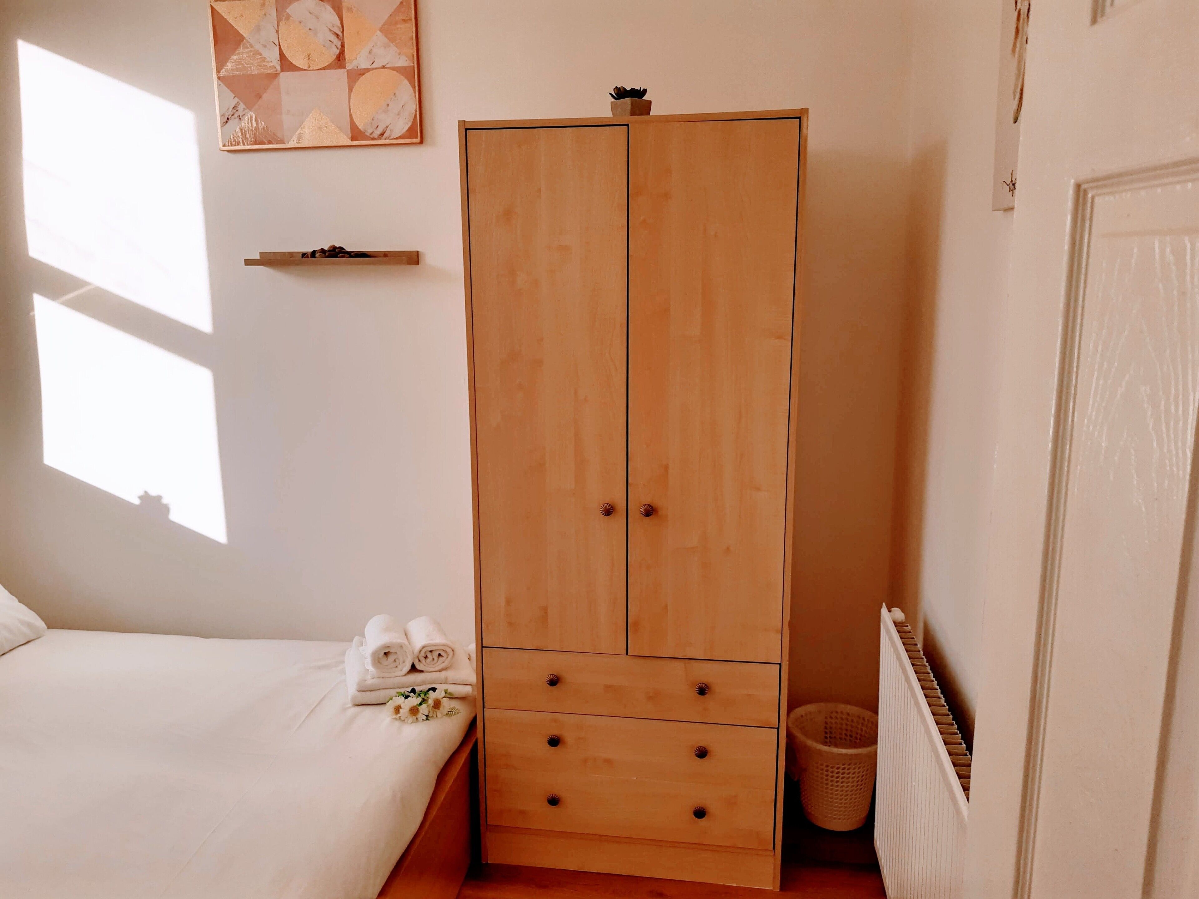 A bedroom with a wooden wardrobe, a bed, and a wall art piece.