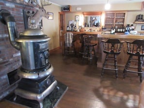 Un rústico área de bar con sillas de madera, una estufa de metal grande y una pared de ladrillo con una decoración de cabeza de ciervo.