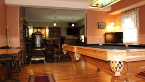 Un tavolo da biliardo in una stanza con pavimento in legno, un'area bar e un televisore.