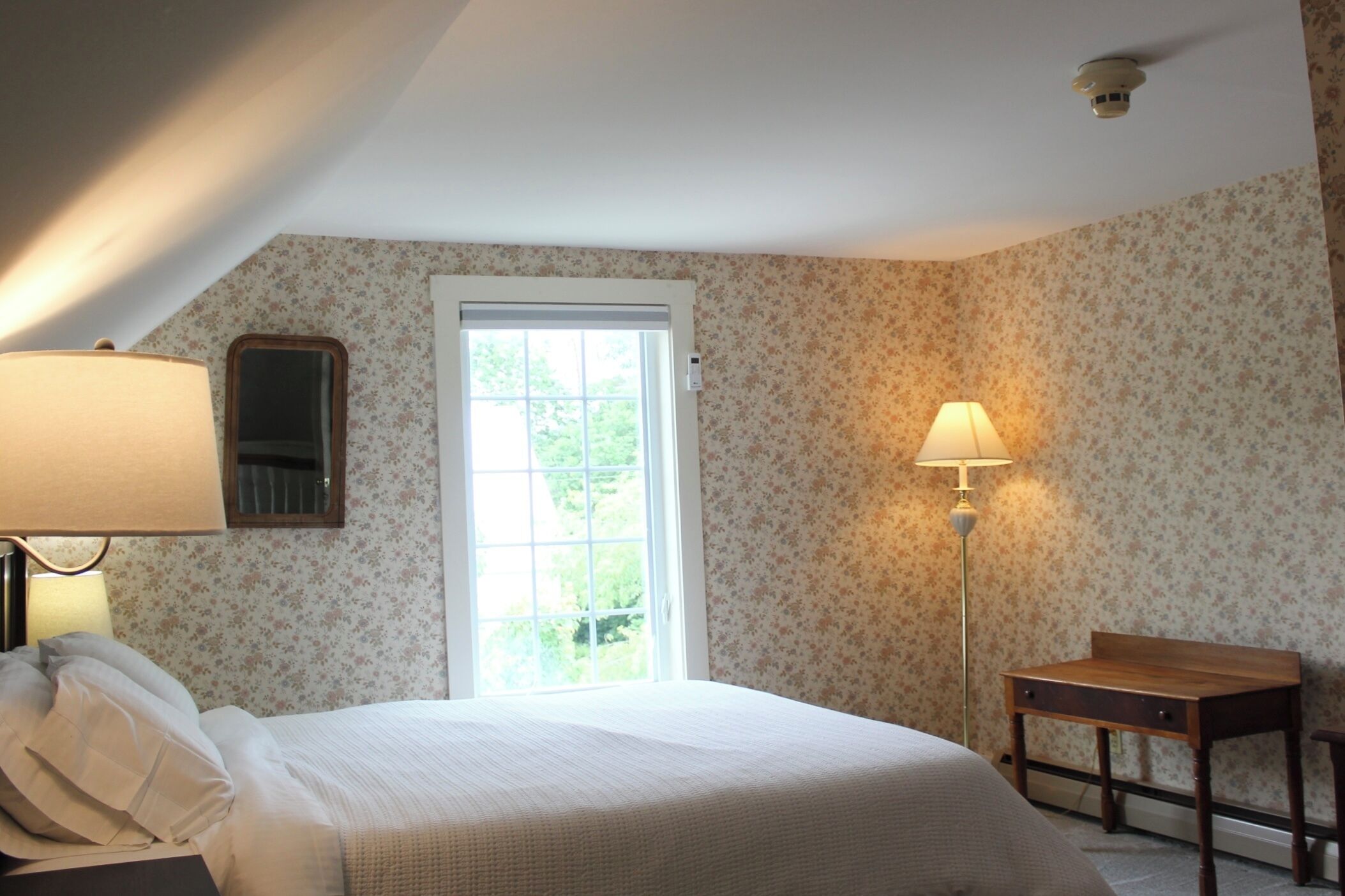 A bedroom with a bed, a desk, a lamp, a window, and a door.