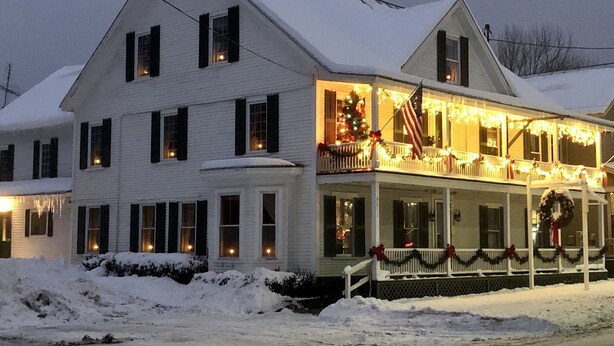 Un edificio bianco di due piani con un portico decorato da luci e ghirlande, circondato dalla neve.