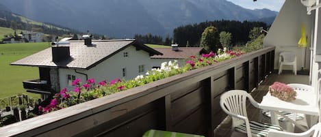 A balcony with a view of mountains, a white chair, a table, and a flower arrangement.