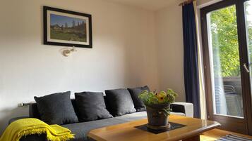 A living room with a sofa, a coffee table, a framed picture on the wall, and a window with curtains.