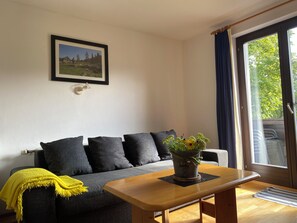 A living room with a sofa, a coffee table, a framed picture on the wall, and a window with curtains.