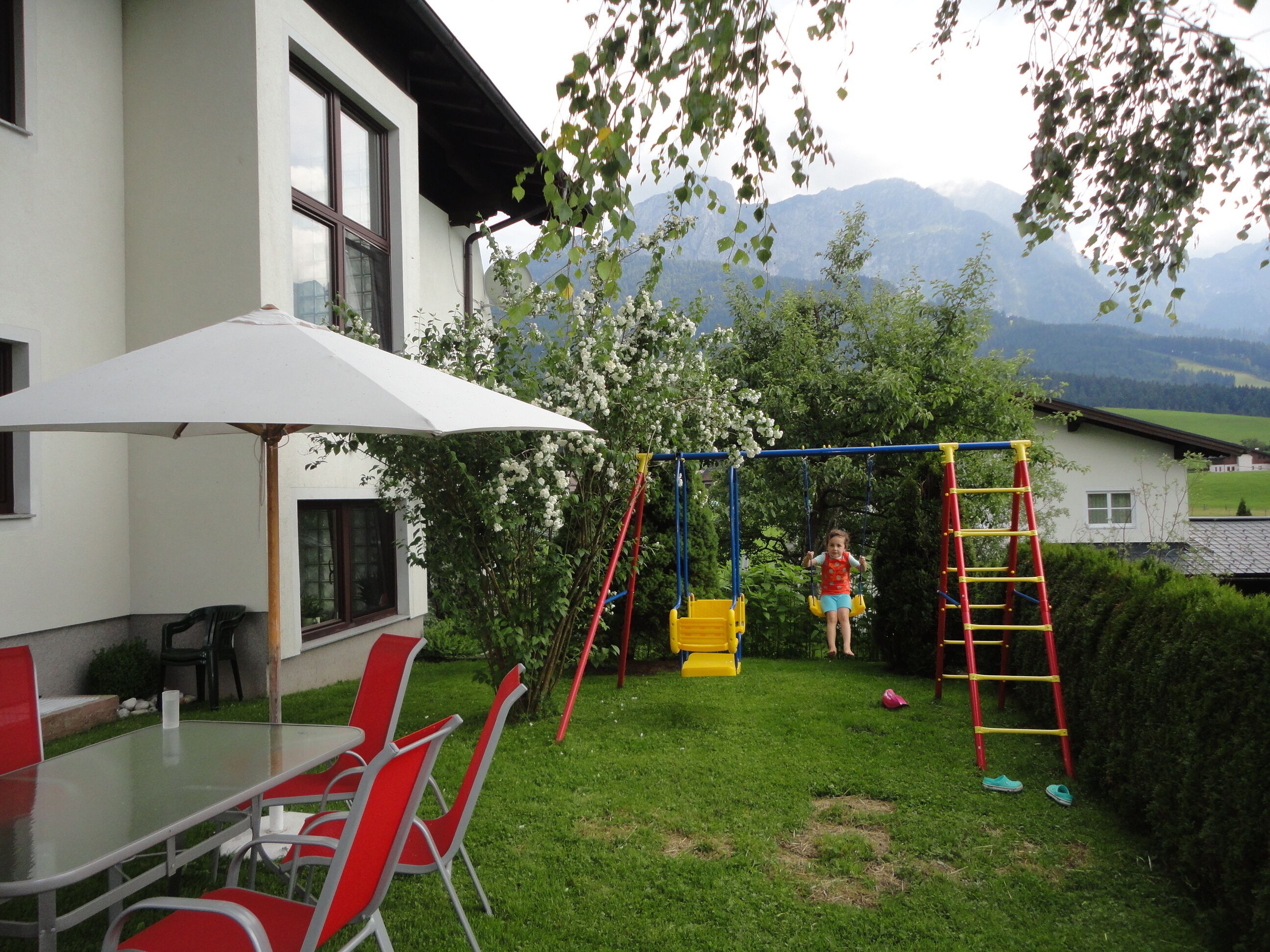 A backyard with a swing set, a table with chairs, and a white umbrella.
