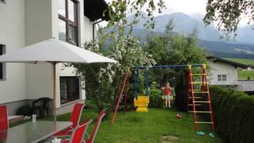 A backyard with a swing set, a table with chairs, and a white umbrella.