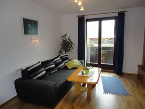 A living room with a sofa, a coffee table, a plant, and a view through a sliding glass door.