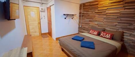 A bedroom with a bed, a wooden headboard, a wall-mounted TV, and a door leading to another room.