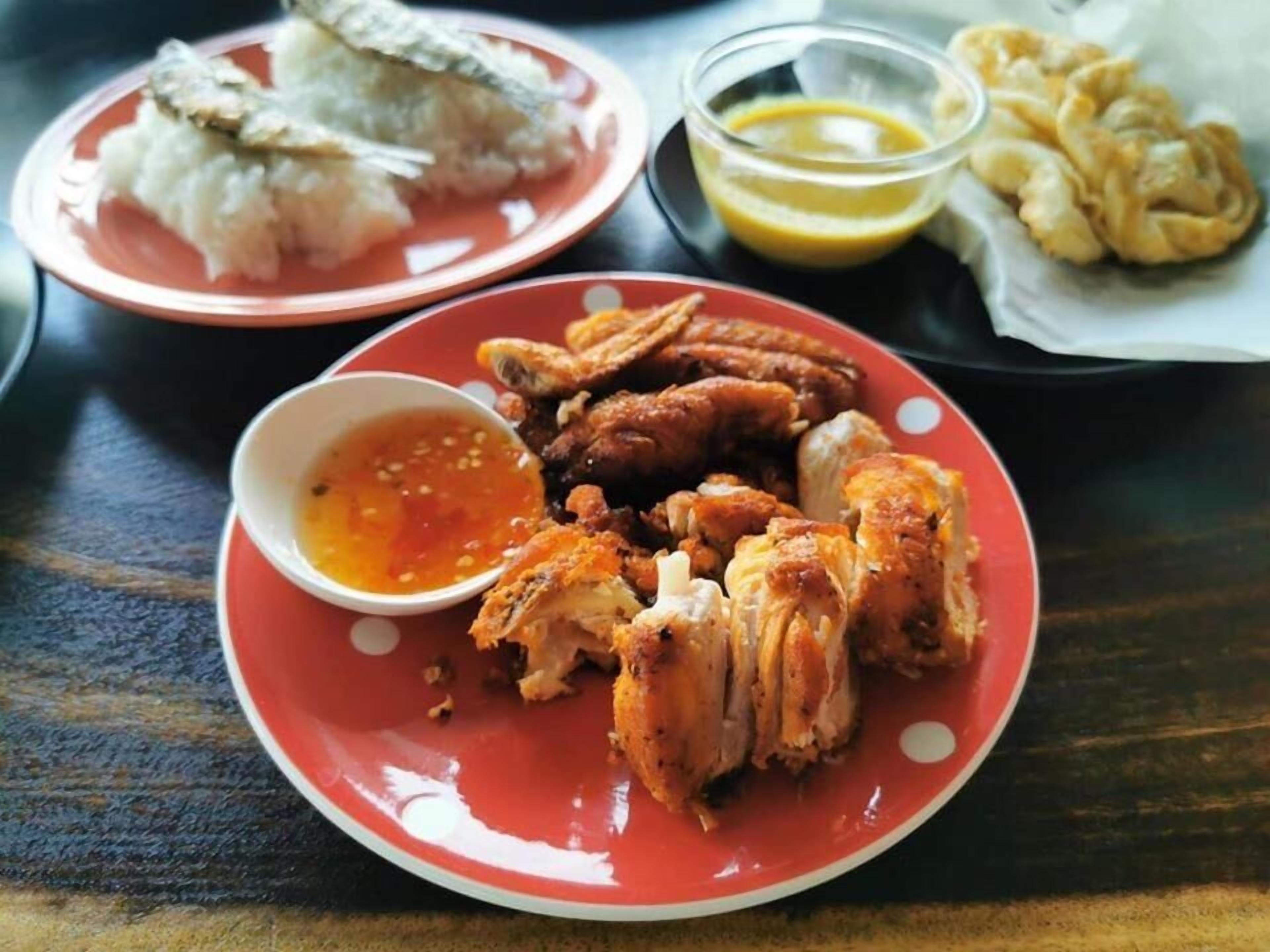 A table with a red plate containing fried chicken, a bowl of sauce, and a plate of fried items.