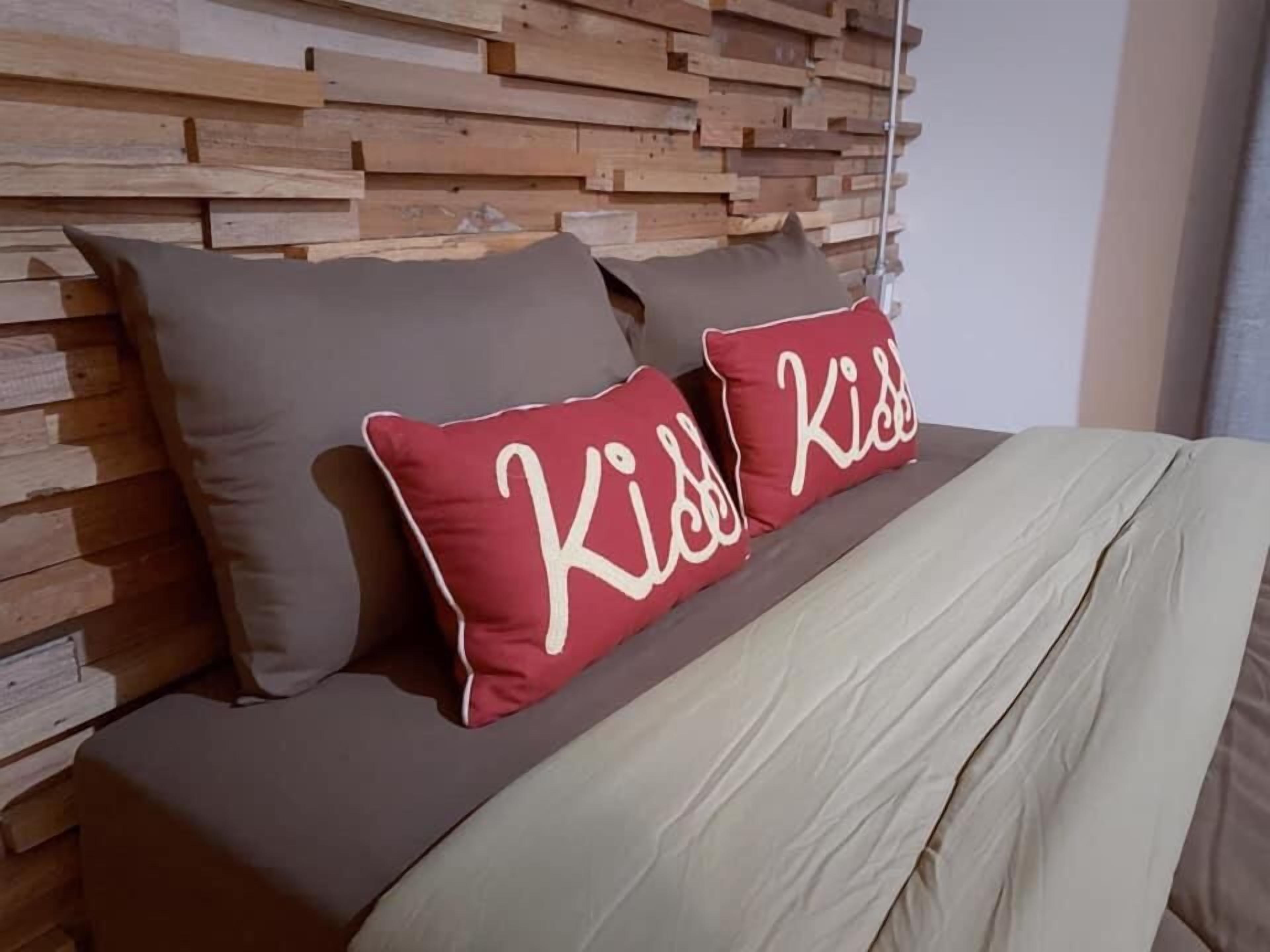 A bed with a wooden headboard, two pillows with the word 'kiss' on them, and a beige bedspread.