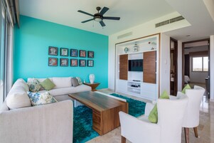 Una sala moderna con una pared de acento color aguamarina, un ventilador de techo, una mesa de centro de madera, un sofá blanco y un sillón blanco.