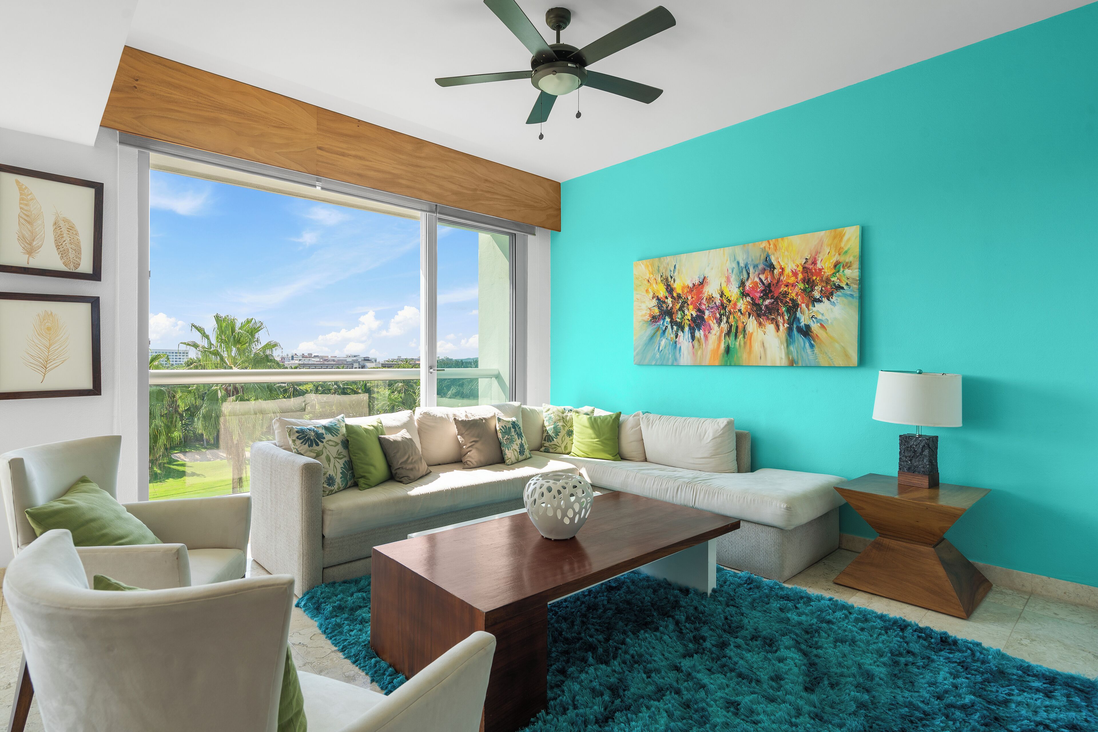 Un salon moderne doté d’une grande fenêtre, d’un ventilateur de plafond et d’un mur d’accent de couleur turquoise.