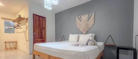 A bedroom with a wooden bed, a macrame wall hanging, a small black cabinet, and a hanging light fixture.