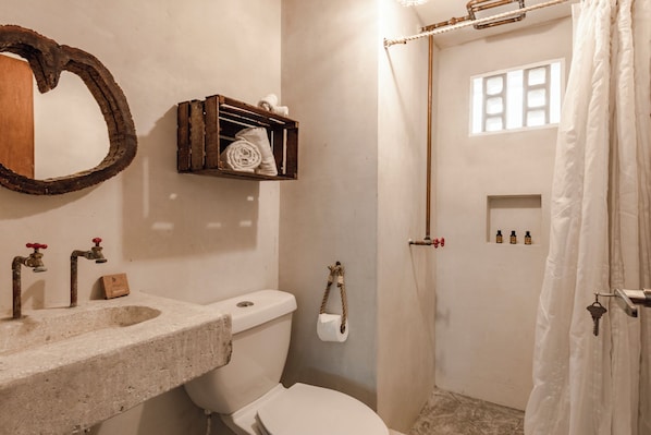 A bathroom with a stone sink, a toilet, a wooden shelf with towels, a mirror, and a shower curtain.