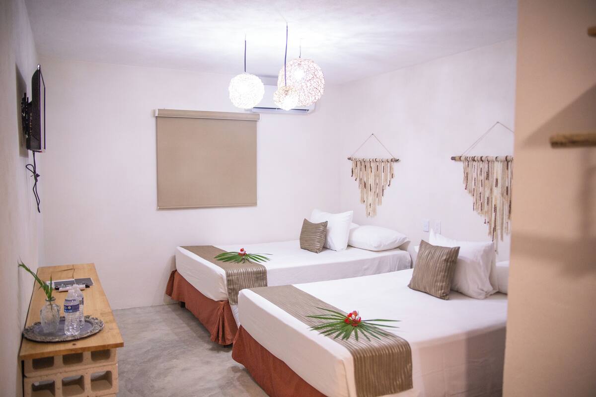 Une chambre d’hôtel avec deux lits, une table en bois, un téléviseur à écran plat et un climatiseur fixé au mur.