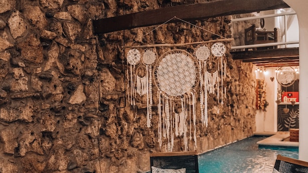 A pool area with stone walls, wooden furniture, and dreamcatchers. - Ahava Hotel (Playa del Carmen)