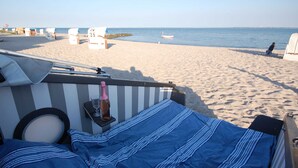 Ein Strandbett mit einer gestreiften blauen Decke, einer Champagnerflasche und einem Glas auf einem kleinen Tisch.