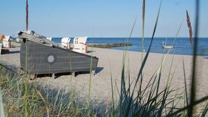 Ein Strand mit einer überdachten Sitzgelegenheit, einem Boot im Wasser und wolkenlosem Himmel.