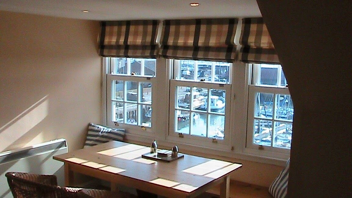 A dining area with a table and chairs, large windows with a view of the city, and a striped valance above the windows.