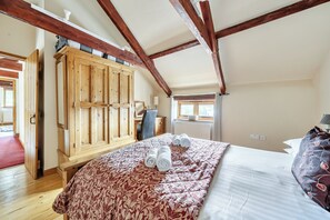 A bedroom with a wooden wardrobe, a bed with a patterned bedspread, and a window with curtains. - Granary Barn, A Rural Retreat - Private Hot Tub, (Winkleigh)