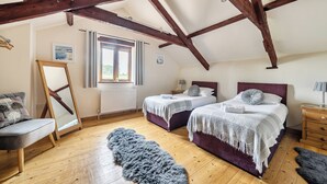 Une chambre avec deux lits, un plancher en bois, une fenêtre et un radiateur.