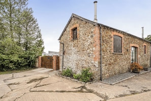 A stone building with a chimney, a wooden gate, and a paved driveway. - Granary Barn, A Rural Retreat - Private Hot Tub, (Winkleigh)
