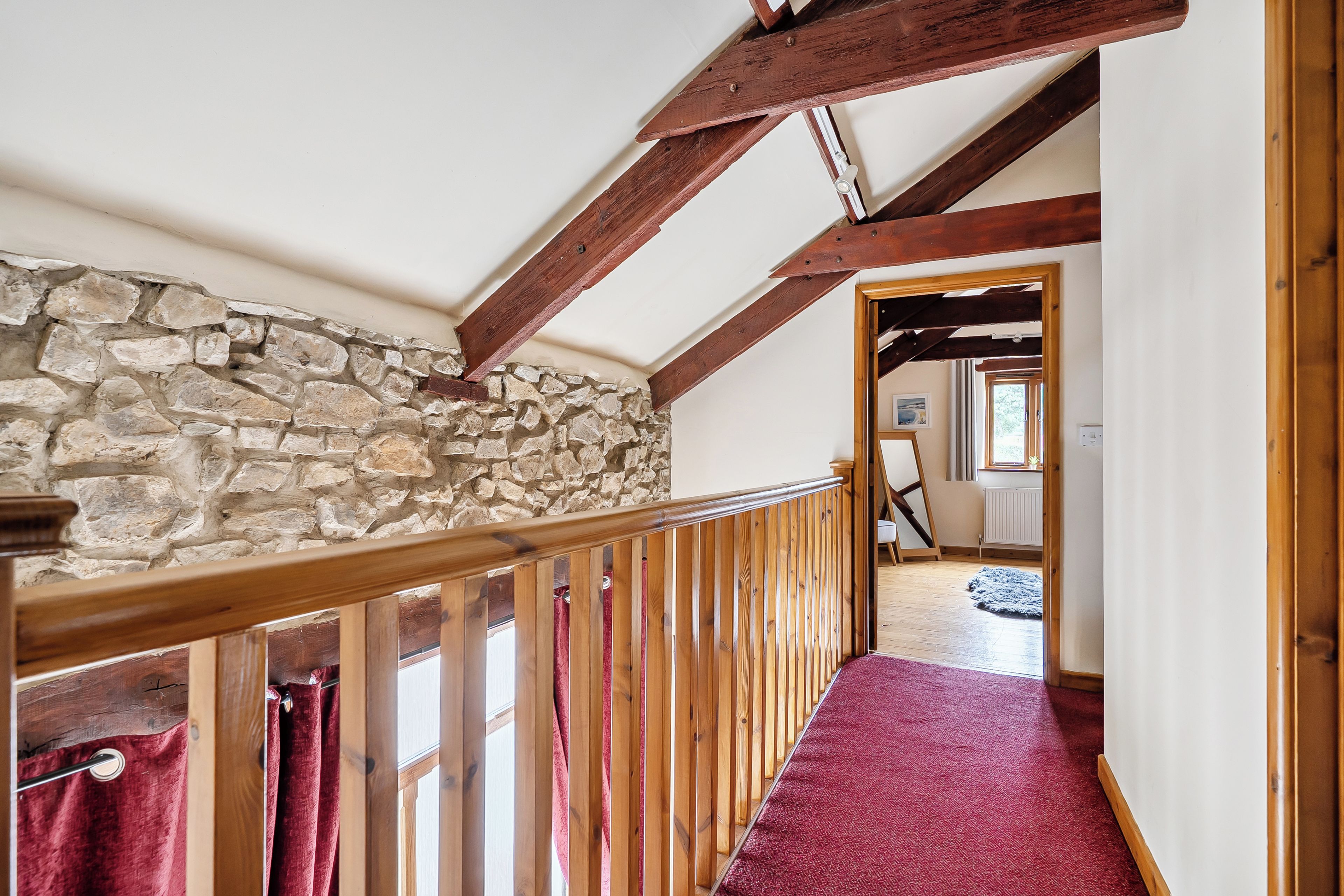 Una escalera de madera con un muro de piedra en un lado y una alfombra roja que conduce a una habitación con ventanal.