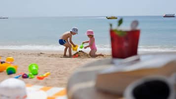 A beach scene with two children playing in the sand, a red cup, and beach toys.