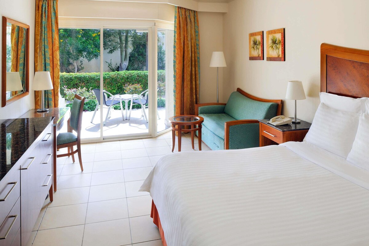 A hotel room with a bed, desk, chair, and a view of the outdoors.