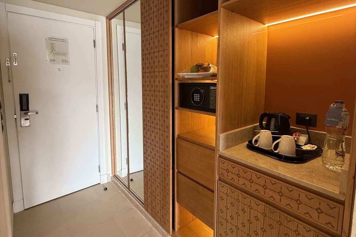 A hotel room with a sliding door, a microwave, a tray with cups and a bottle, and a water dispenser.