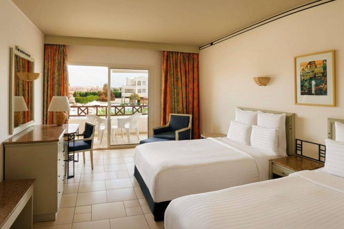 A hotel room with two beds, a desk, a chair, and a balcony with a view.