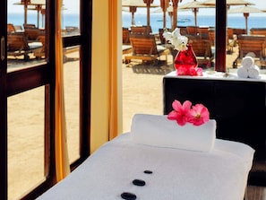 A spa area with a massage table, a vase with flowers, and a view of the beach through large windows. - Naama Bay Promenade Beach Resort by Accor (Sharm El Sheikh)