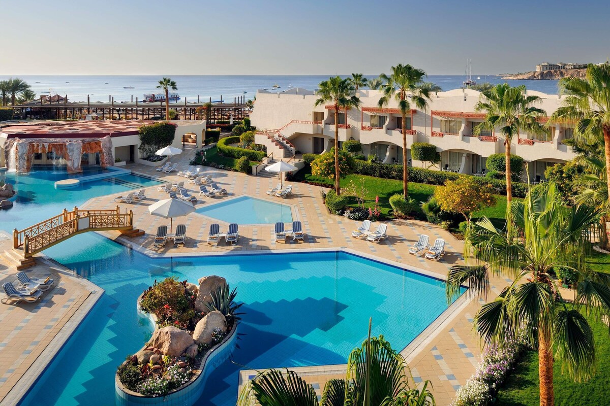 A resort with a large swimming pool, sun loungers, and a view of the sea.