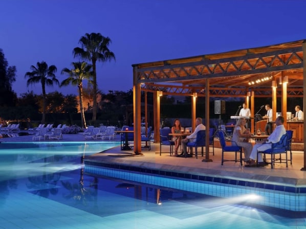 Un espace aménagé au bord de la piscine, avec des chaises longues et un coin salon couvert où un groupe de musique se produit.