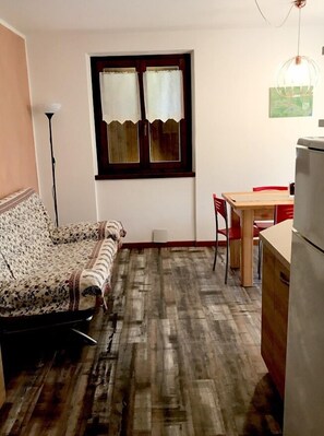 A compact living space with a sofa, a dining table, and a refrigerator. - Residence Alessio (Ledro)